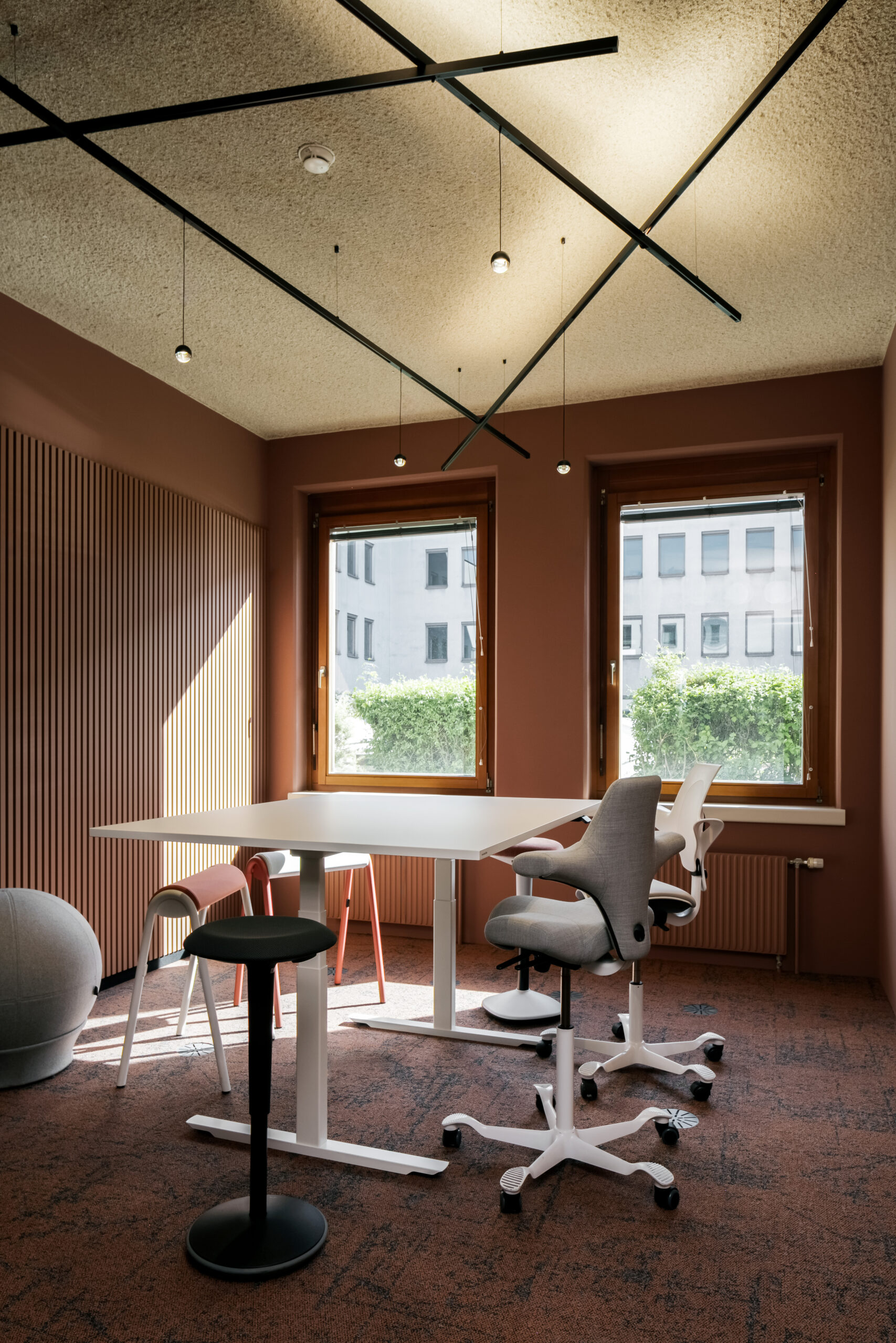 Innenansicht eines modernen Büros mit einem weißen Tisch, verschiedenen Stühlen und einem warmen, erdigen Farbton an den Wänden. Das Lichtdesign betont die offene Atmosphäre.